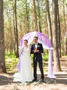 Wonderful stylish rich happy bride and groom standing at a wedding ceremony in green garden near purple arch with Royalty Free Stock Photo