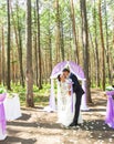 Wonderful stylish rich happy bride and groom standing at a wedding ceremony in green garden near purple arch with Royalty Free Stock Photo