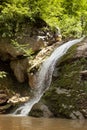 Wonderful summer waterfall in mountain with lush green forest, layered rocks overgrown moss and bright sunbeams on mountain river. Royalty Free Stock Photo