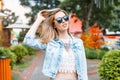 Wonderful young hipster woman in a stylish blue denim jacket in black sunglasses in a vintage lace blouse with a necklace Royalty Free Stock Photo