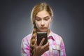 Wondering girl looking at mobile phone or cellphone. Closeup Portrait of teen in casual shirt on grey background Royalty Free Stock Photo