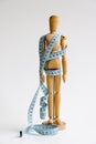 Wood mannequin holding and wrapped in a blue tape measure for a weight loss and plastic surgery beauty concept