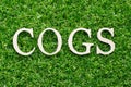 Wood alphabet in word COGS Abbreviation of Cost of goods sold on green grass background Royalty Free Stock Photo