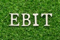 Wood alphabet in word EBIT Abbreviation of Earnings Before Interest and Taxes on green grass background