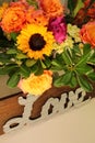 wood behind a ripple metal LOVE sign, fall flower arrangement (sunflowers, peach roses, purple flowers