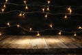 wood board table in front of Christmas warm gold garland lights on wooden rustic background. Royalty Free Stock Photo
