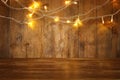 wood board table in front of Christmas warm gold garland lights on wooden rustic background. glitter overlay Royalty Free Stock Photo
