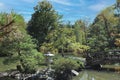 A wood bridge leading to a small island in a lake with evergreens, shrubs and a Japanese stone lantern Royalty Free Stock Photo