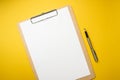 Wood clipboard with empty white paper and pen isolated on yellow background