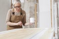Wood crafts, woman artisan carpenter painting with brush and paint jar white the door in workshop, wearing overall and eyeglasses