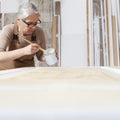 Wood crafts, woman artisan carpenter painting with brush and paint jar white the door in workshop, wearing overall and eyeglasses