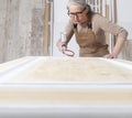 Wood crafts, woman artisan carpenter painting with spray gun paint white the door in her workshop, wearing overall and eyeglasses