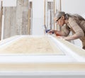 Wood crafts, woman artisan carpenter painting with spray gun paint white the door in her workshop, wearing overall and eyeglasses