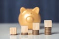 Wood cube on coins stack, gold piggy bank background