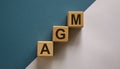 Wood cubes with acronym `AGM` - `annual general meeting` on a beautiful white and blue background. Business concept, copy spac