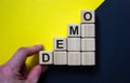 Wood cubes with word `demo` stacking as step stair on paper black and yellow background, copy space. Male hand. Business concept