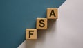 Wood cubes with word `FSA, flexible spending account` stacking as step stair on paper blue and white background, copy space. Royalty Free Stock Photo