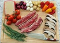 Wood cutting board in kitchen table with beef short ribs, rosemary, mushrooms, tomatoes, cheese, onions and peppers.