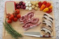 Wood cutting board in kitchen table with raw lamb ribs red meat, rosemary, mushrooms, tomatoes, cheese, onions and peppers.