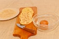 Wood cutting board with a knife and three slices of peeled eggplant with a bowl of breadcrumbs, and glass bowl with two rows eggs