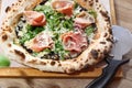 Wood fired Italian pizza with prosciutto, parma ham, arugula, and parmesan, on a wooden cutting board, top view. Royalty Free Stock Photo