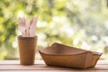 Wood forks and knives in craft cups, paper plates, natural green blurred background. Eco-friendly disposable kitchenware utensils