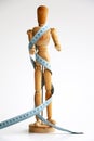 Wood mannequin holding and wrapped in a blue tape measure for a weight loss and plastic surgery beauty concept