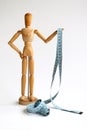 Wood mannequin holding and wrapped in a blue tape measure for a weight loss and plastic surgery beauty concept