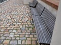 Wood-paneled benches by a bright plaster wall in a park sunk with leaves and creepers other clean and tidy around. cubes paving gr