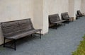 Wood-paneled benches by a bright plaster wall in a park sunk with leaves and creepers other clean and tidy around. cubes paving gr