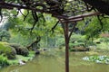 A wood pergola built over a large pond, covered in tree branches in a landscaped Japanese Garden in Seattle, Washington