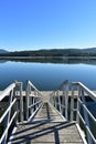 Wood pier and stairs in a bay with water reflections. Forest and beach. Blue sky, sunny day. Galicia, Spain.