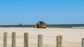 Wood piling posts near beach with yellow road grader leveling sand Royalty Free Stock Photo