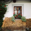 Wood stacks and idyllic cottage window with red flowers, preparing for winter