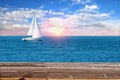 Wood table looking at ocean with sunset and a sailboat