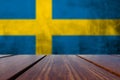 Wood Table Top and Grunge Sweden Flag on concrete wall.