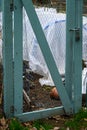 Wood and wire mesh gate into a winterized kitchen garden, plants covered with plastic