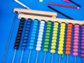 Wooden abacus with multicolored beads on a bright blue surface among colored pencils Royalty Free Stock Photo
