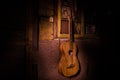 An wooden acoustic guitar is against a grunge textured wall. The room is dark with a spotlight for your copyspace Royalty Free Stock Photo