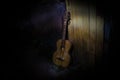 An wooden acoustic guitar is against a grunge textured wall. The room is dark with a spotlight for your copyspace Royalty Free Stock Photo