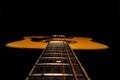 Wooden acoustic guitar with fretboard and strings over black studio background. Stringed plucked musical instrument