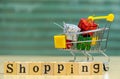 Wooden Alphabet words `shopping` and shopping cart with full of presents or gifts in front of the Blur Shopping Store