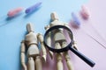 Wooden anthropomorphic mannequins of a man and a woman and a magnifying glass on a gendered pink and blue background. Concept of