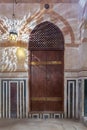 Wooden arched door on stone wall decorated with marble panels and lantern shadows on the wall, Old Cairo, Egypt