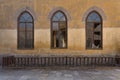 Wooden arched window with wrought iron grid over yellow stone bricks wall and wooden balustrade Royalty Free Stock Photo