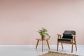 Wooden armchair with gray upholstery and a side table in a pastel pink living room interior with place for a bookcase. Real photo. Royalty Free Stock Photo