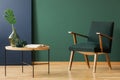 Wooden armchair next to table and book in green and blue living room interior. Real photo