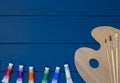 Wooden art palette with paints and brushes on classic blue wooden background. Close up of tubes with oil paints on the table. Royalty Free Stock Photo