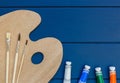 Wooden art palette with paints and brushes on classic blue wooden background. Close up of tubes with oil paints on the table. Royalty Free Stock Photo