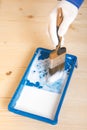 On a wooden background, blue bath with white paint and the hand of a master with a brush in a glove, close-up Royalty Free Stock Photo